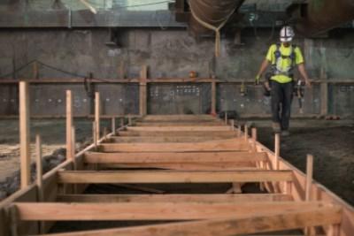 Worker in safety gear inspecting wooden concrete forms in underground transit station construction.