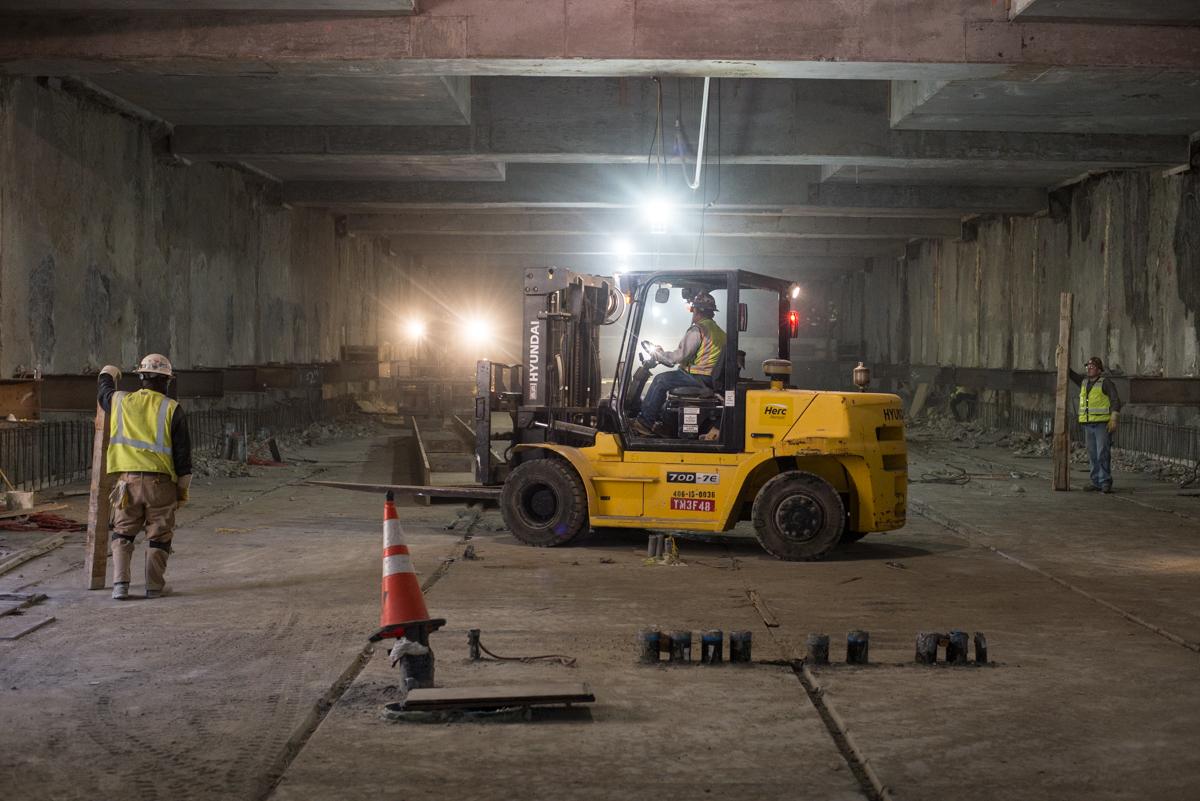 Workers operate a forklift to move steel I-beam inside an underground transit station under construction.
