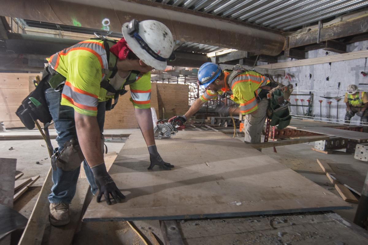 Construction workers in safety gear cut plywood for concrete forms inside Union Square/Market Street Station.