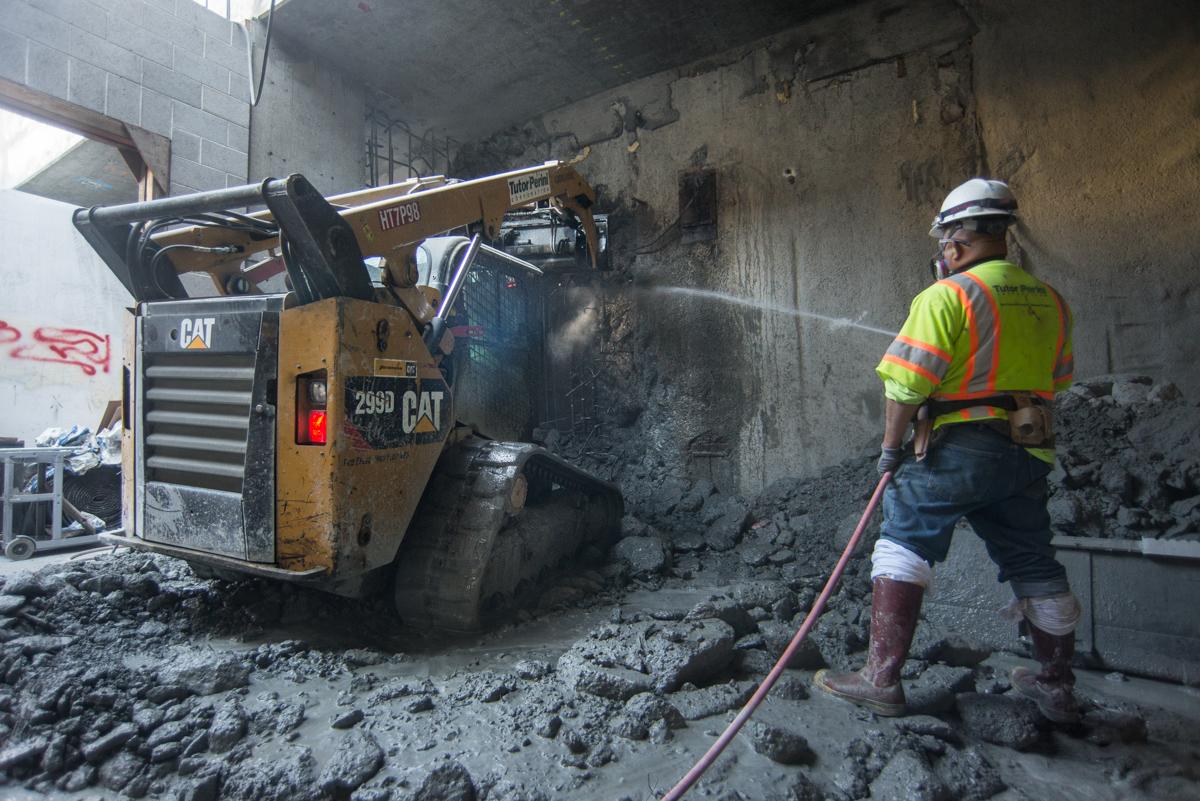 Worker sprays water while equipment breaks up concrete during underground construction work.