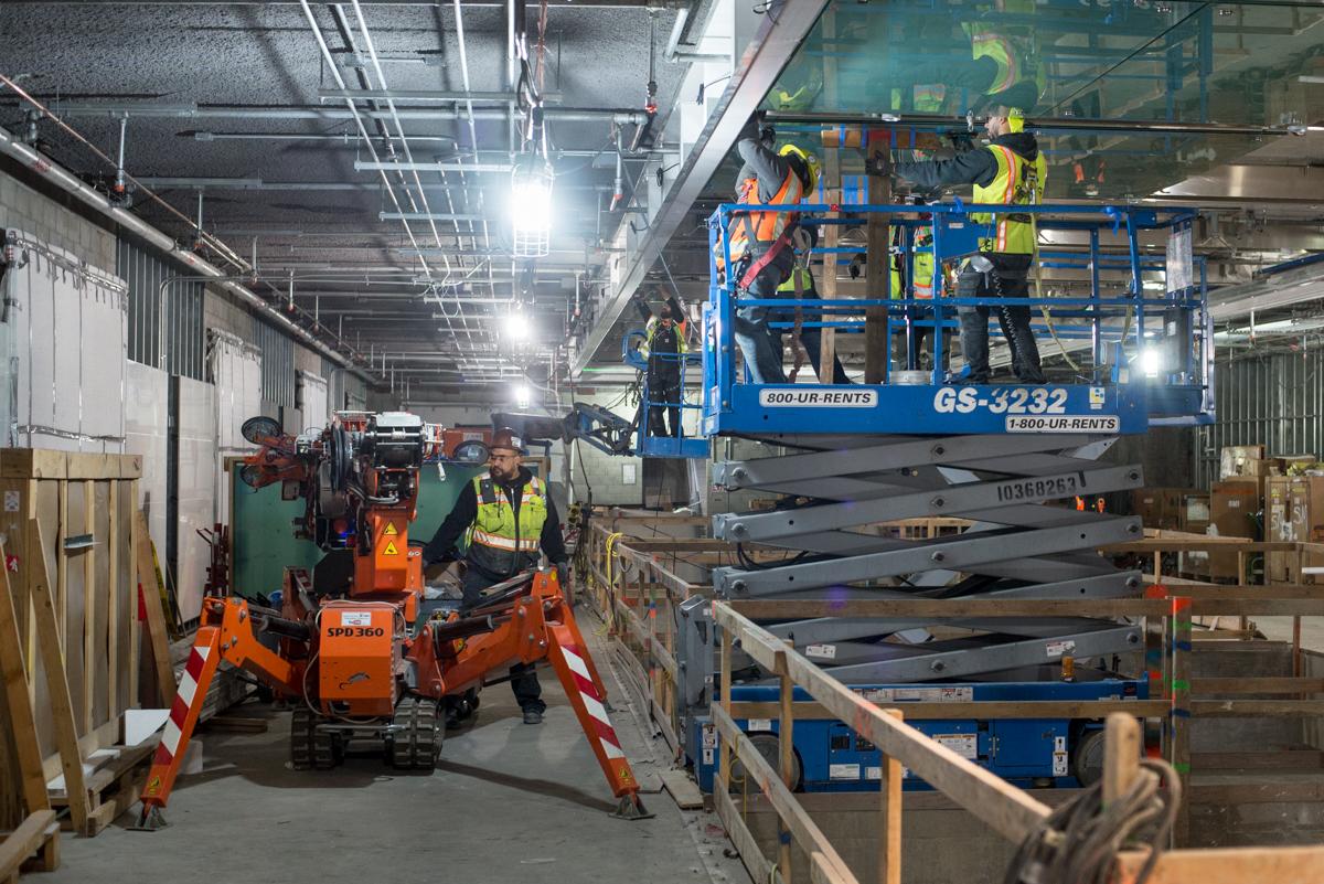 Workers on blue scissor lift and orange equipment performing maintenance in industrial warehouse facility.