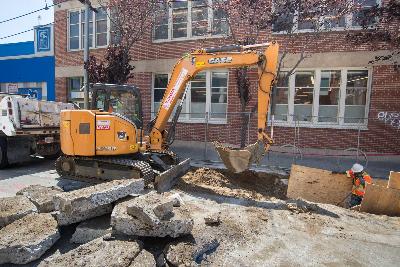 Yellow excavator removing soil during trenching operations on 4th Street for utility installation work.