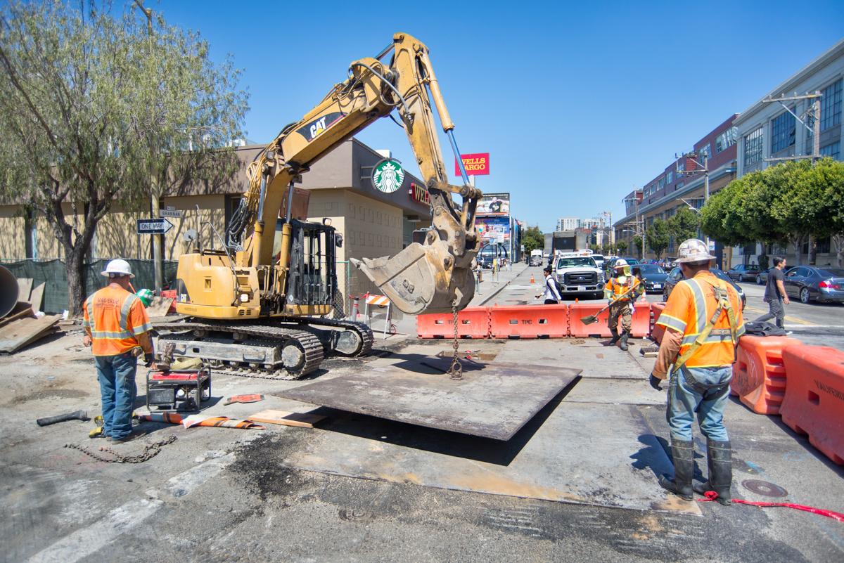Construction crew operates excavator at street work site on 4th Street for transit project.