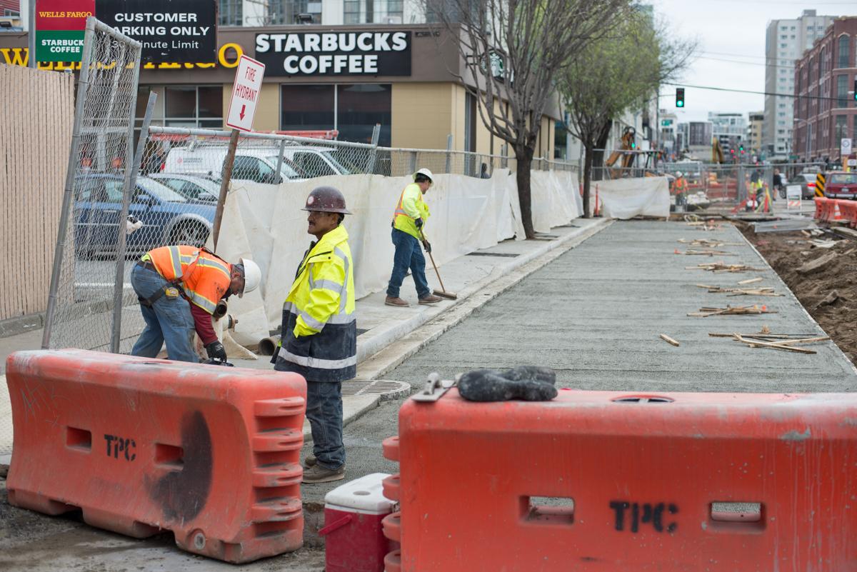 Construction workers in safety vests repair street infrastructure near Starbucks on 4th Street.