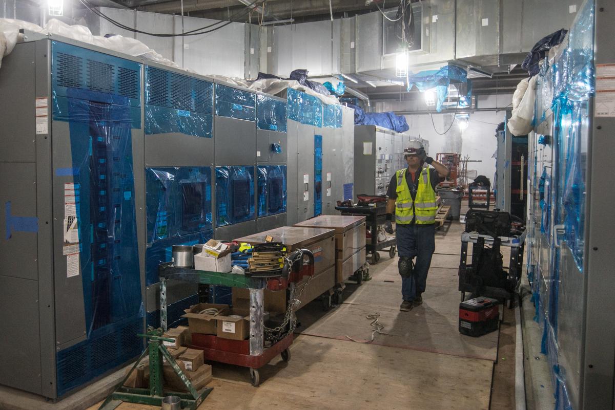 Worker in safety vest walks through underground transit station under construction with blue-wrapped equipment and structural installations.