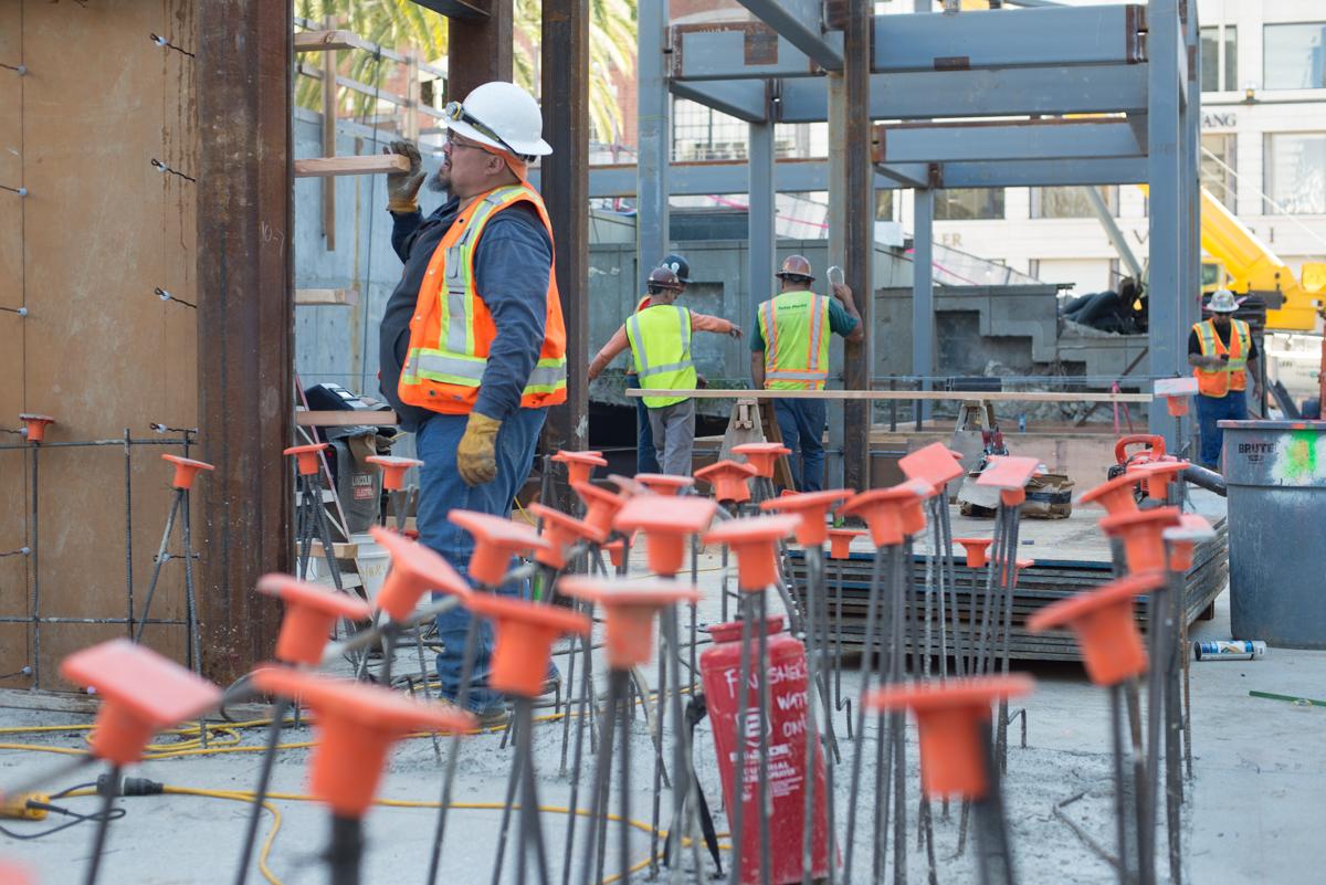 Construction workers in safety gear and orange warning flags mark an active work zone on a city street.