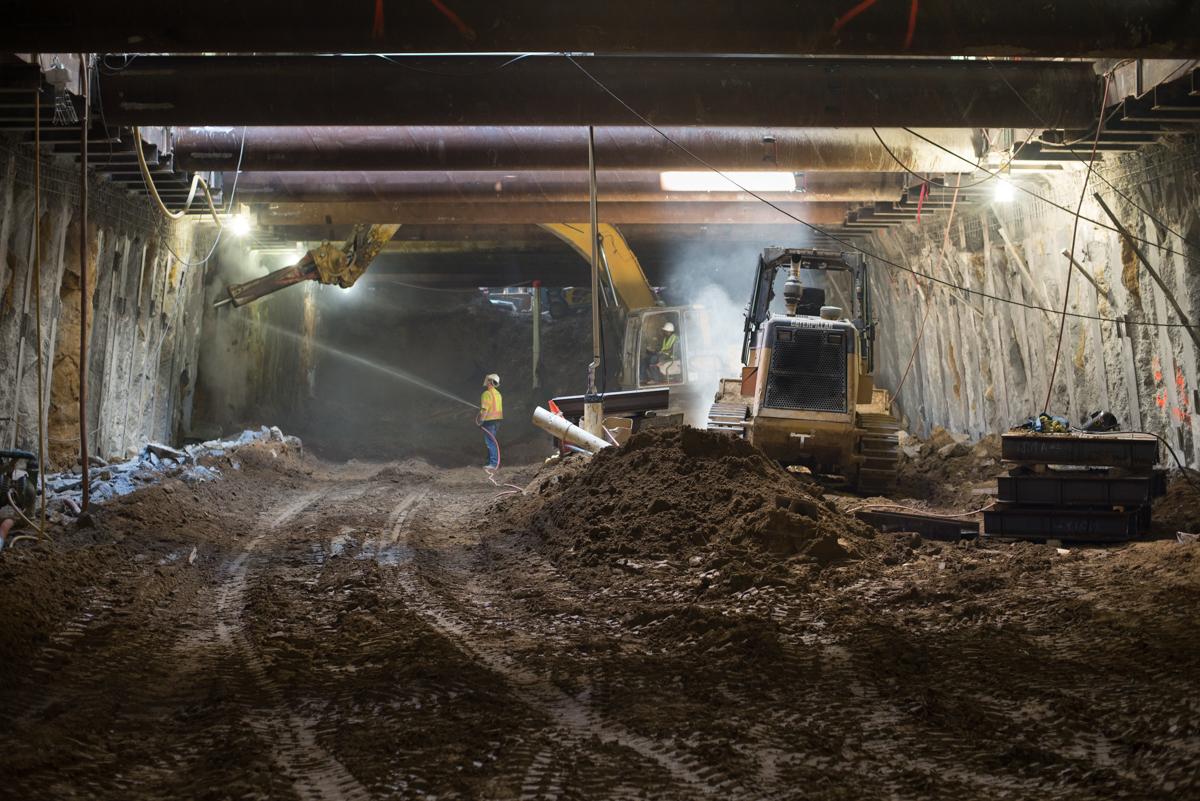 Underground tunnel excavation with heavy equipment and workers removing concrete from station walls.