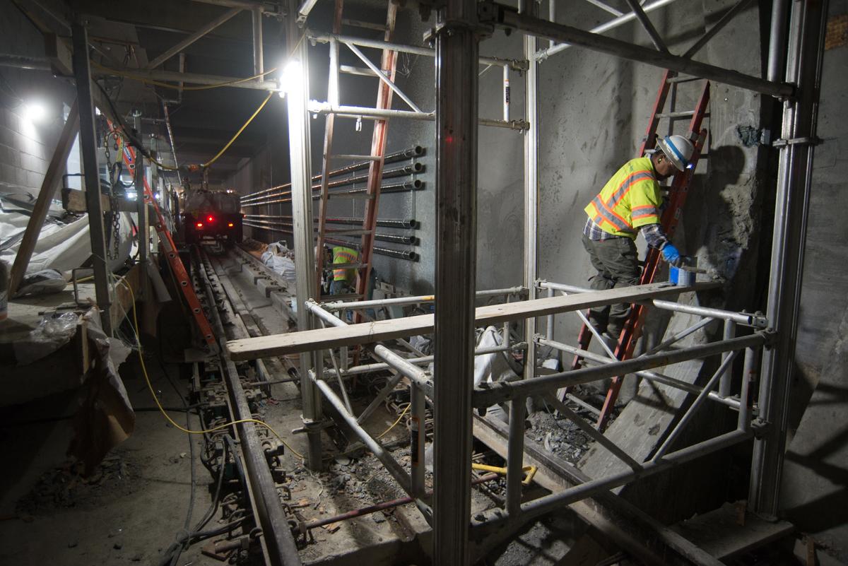 Worker in safety vest repairs concrete at underground transit tunnel entrance at night.