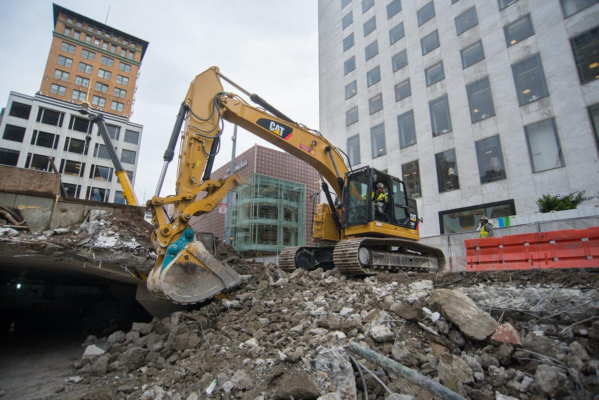 Yellow CAT excavator removing debris at Union Square construction site surrounded by downtown buildings.