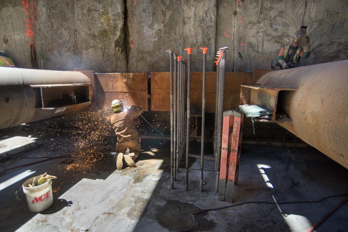Worker welding reinforcing steel inside concrete tunnel structure during construction.