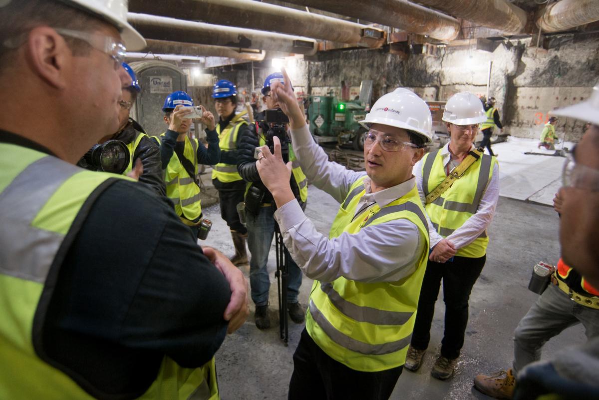 Construction workers and officials in safety vests and hard hats tour an underground transit station.
