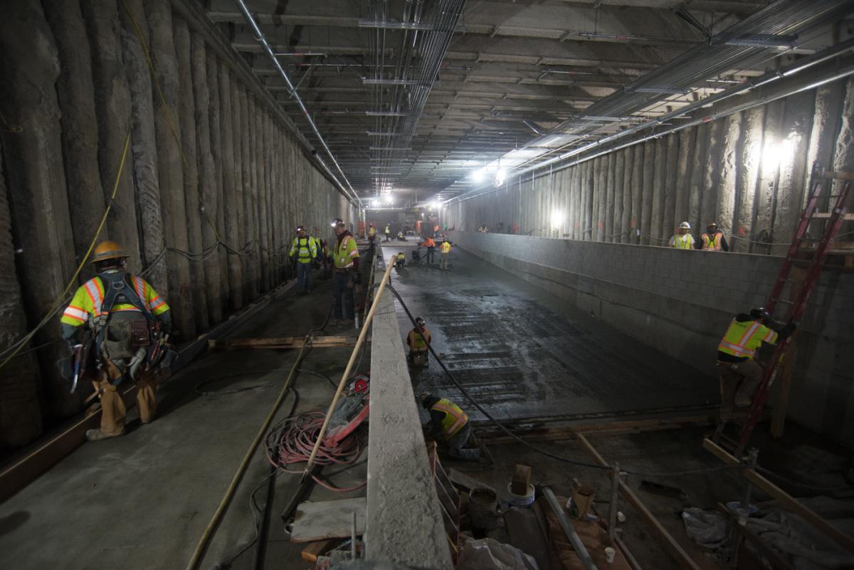 Workers in safety vests pour concrete for the transit station concourse floor slab.