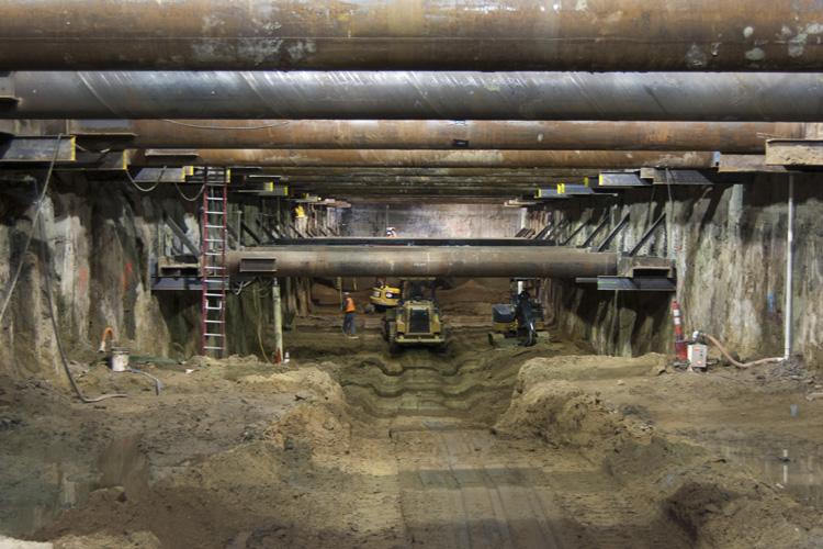 Construction excavation beneath 4th Street showing tunnel launch box with heavy equipment and support structures.
