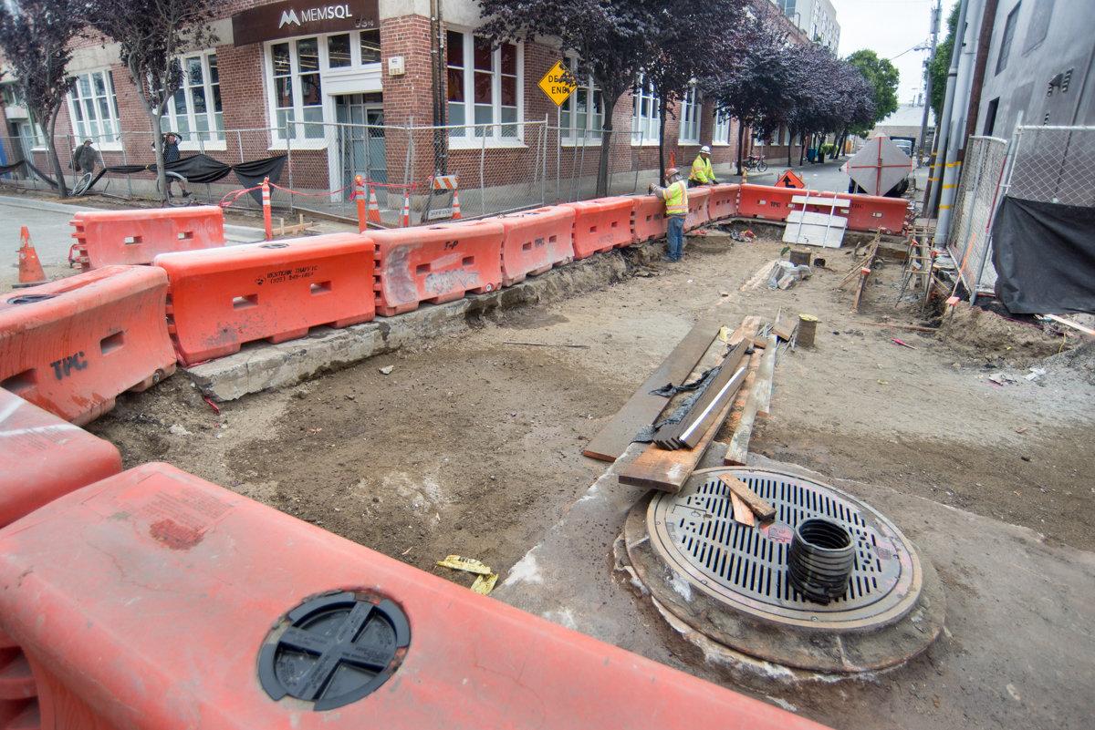 Construction site with red barriers, excavation, and sewer infrastructure work on urban street.