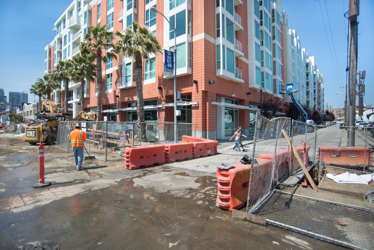 Construction site at Central Subway station with orange barriers, workers, and new residential building in background.