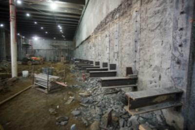 Construction site showing concrete wall demolition and steel support beams in underground transit concourse.