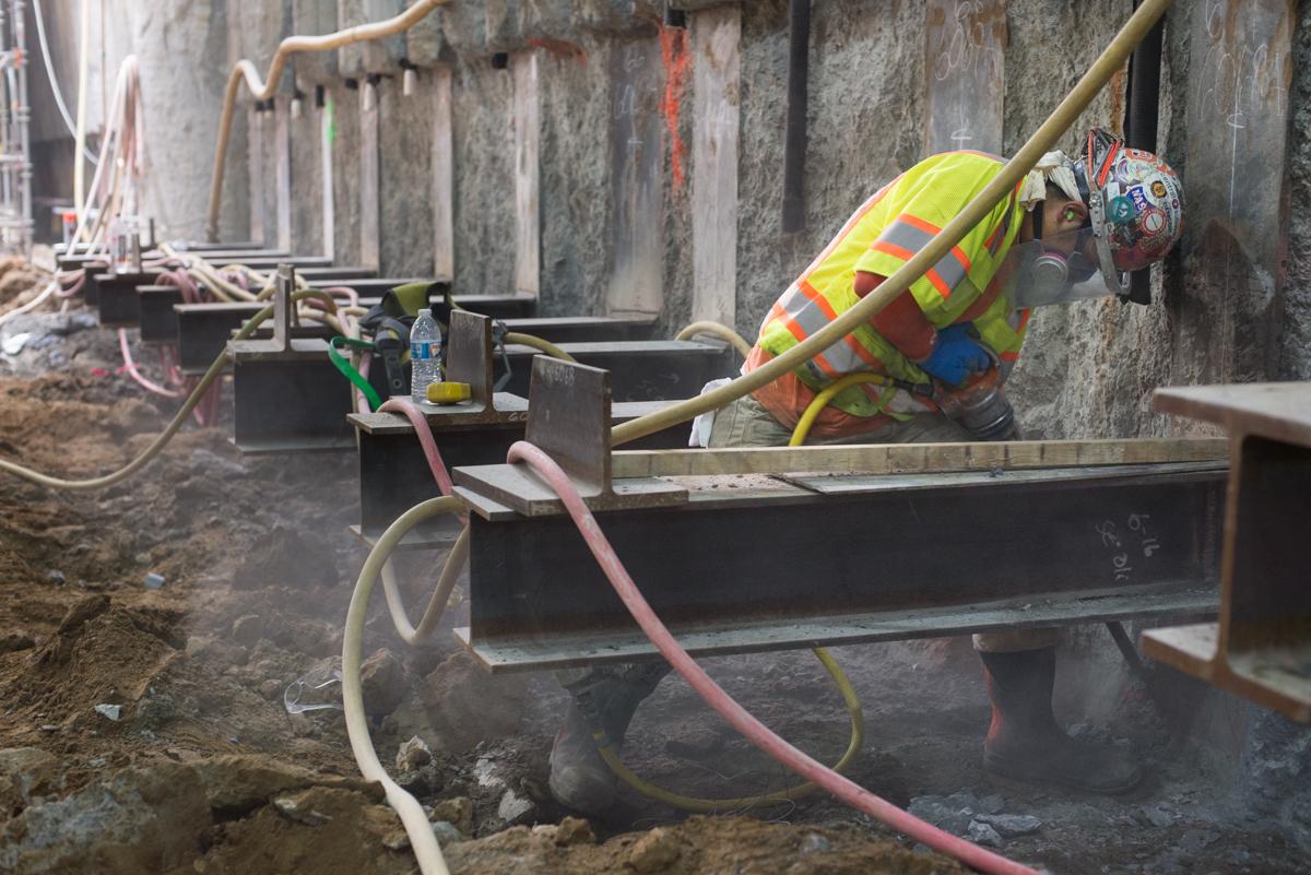 Construction worker in safety vest and hard hat applying concrete to underground tunnel wall with hose.