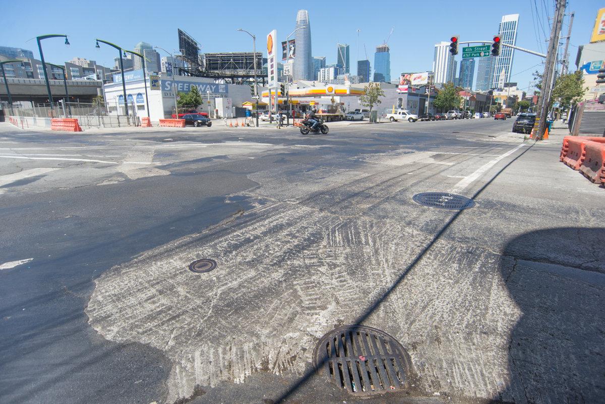 Urban intersection with construction work, street repairs visible, San Francisco skyline in background.