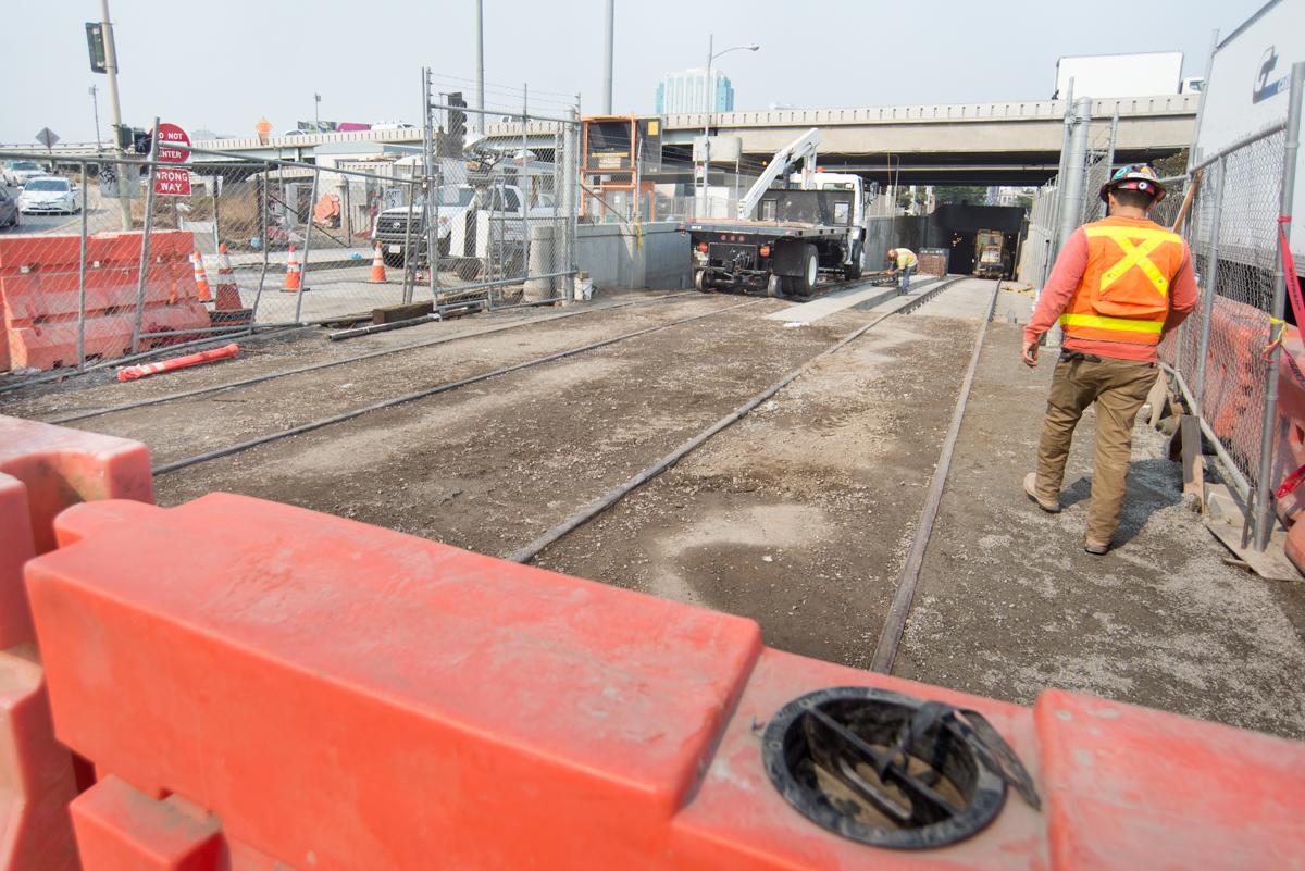 Construction worker in safety vest walks through transit tunnel worksite with equipment and vehicles.
