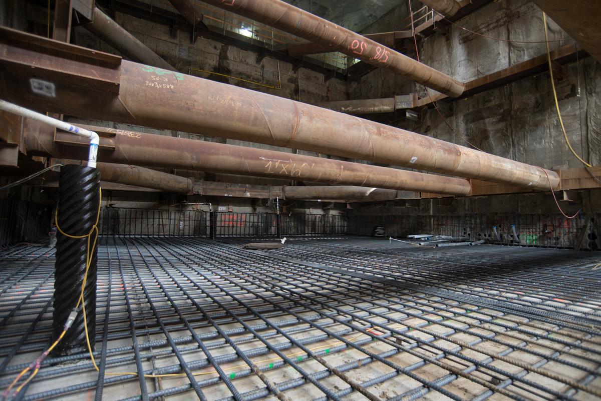 Large steel pipes suspended above reinforced concrete foundation with rebar grid at station construction site.