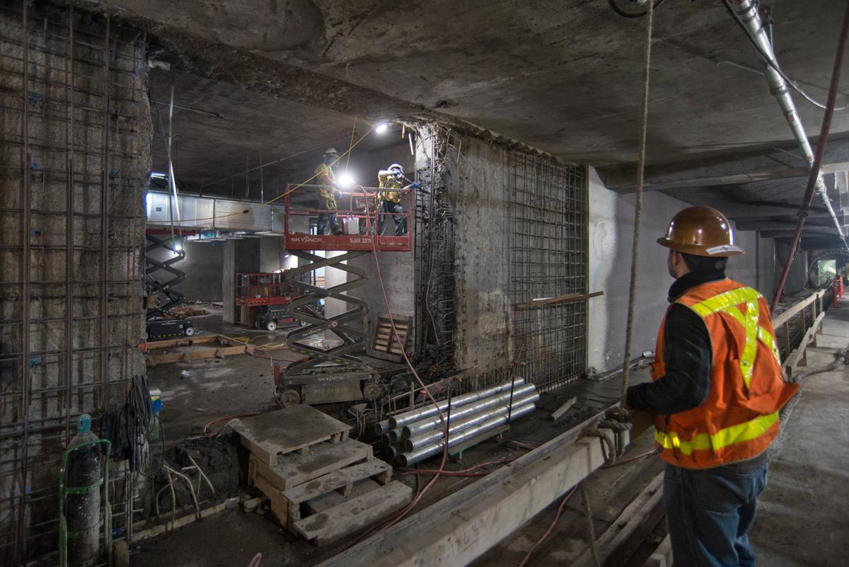 Construction worker in safety vest observing concrete formwork and temporary bracing installation in underground transit station.