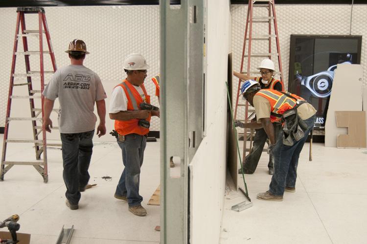 Construction workers in safety vests and hard hats build a wall at Powell Street Station entrance.
