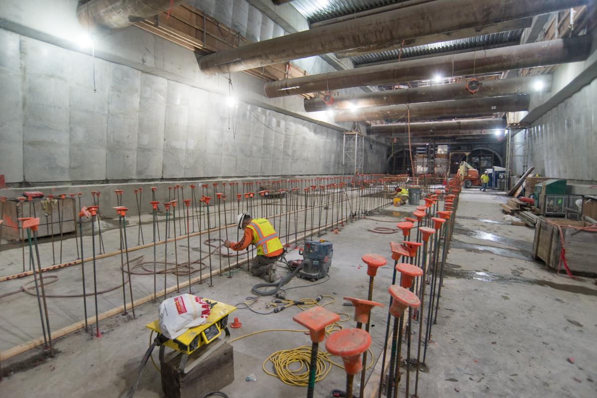 Construction workers install rebar framework inside underground transit station box.