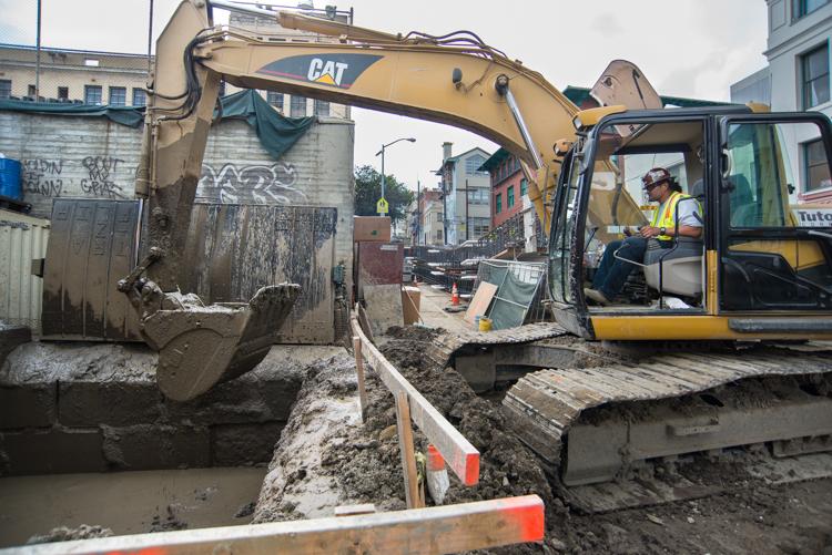 CAT excavator operator digging slurry walls at Ellis Street construction site in Chinatown.