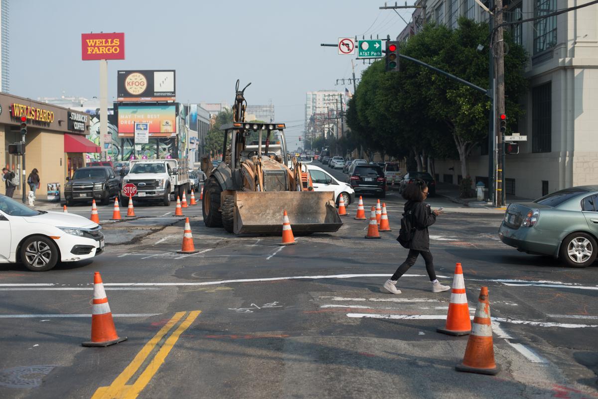 Construction equipment and traffic cones block an urban intersection during daytime street work.
