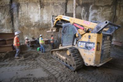 Yellow CAT skid steer loader operating on 4th Street construction site with workers nearby.