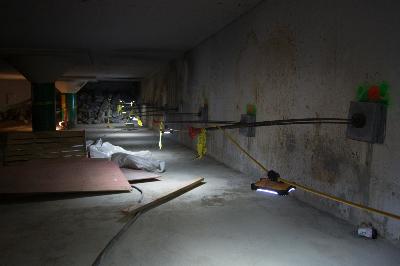 Underground construction site with exposed drainage pipe and steel tiebacks along concrete wall.