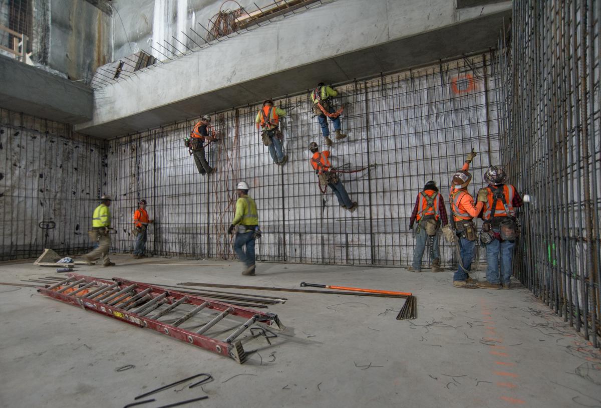 Workers in safety gear practice rope descent training on an interior concrete wall with metal mesh during transit station construction.