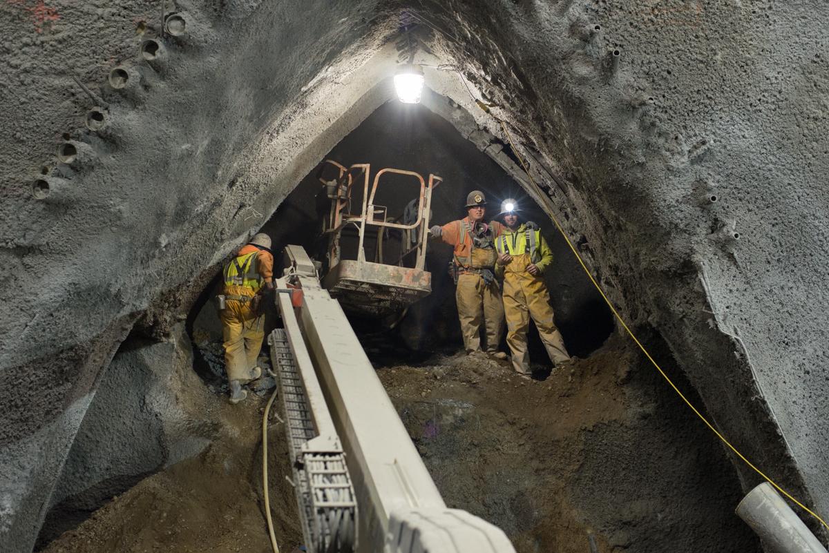 Workers in safety gear install reinforcement and shotcrete in an underground transit tunnel excavation.