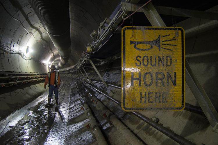 Worker in safety vest stands in tunnel with yellow sound horn warning sign visible on wall