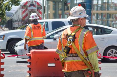 Construction workers in safety vests and hard hats survey a street work zone near Caltrain Station.