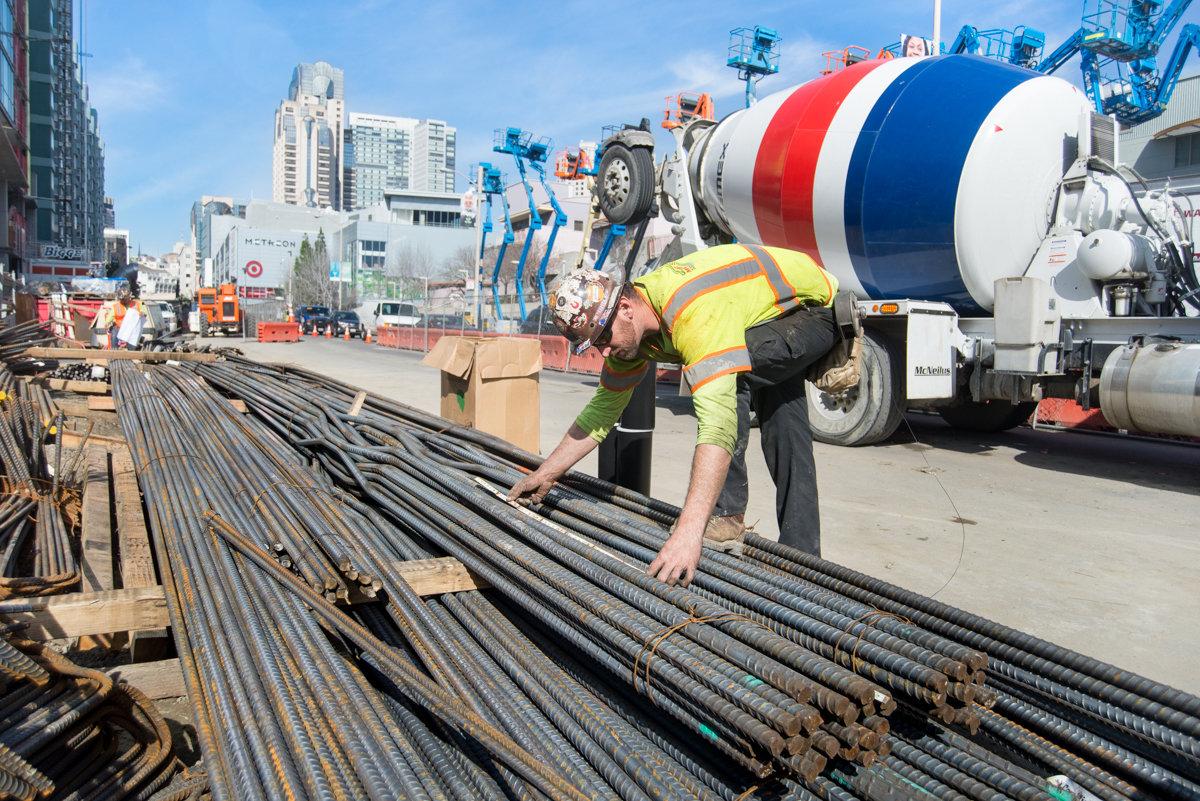 Construction worker inspecting rebar steel reinforcement bars at transit station work site.
