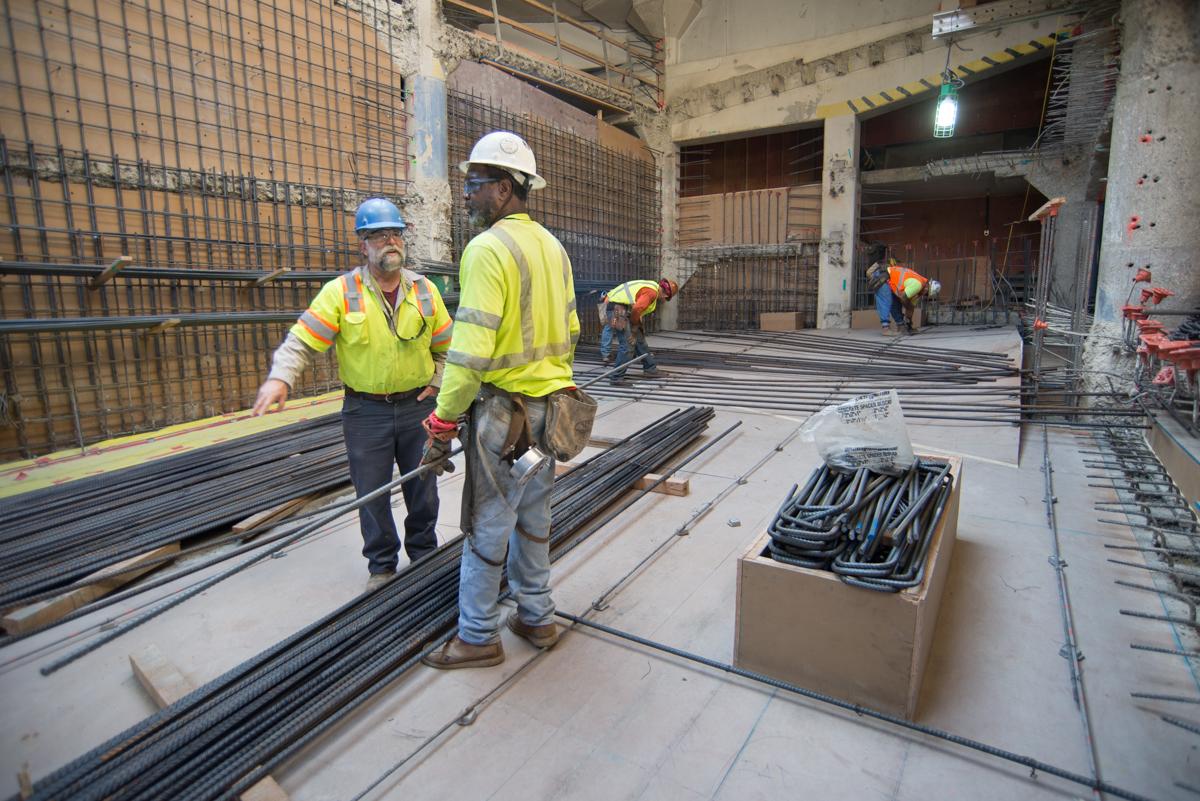 Construction workers installing rebar and steel reinforcement materials inside a parking garage structure.