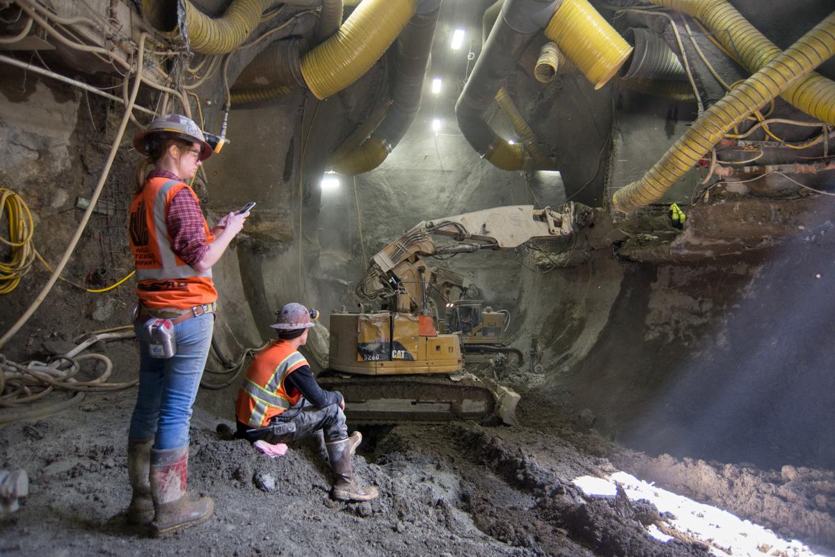 Workers in safety gear operate an excavator in an underground tunnel during construction or repair work.