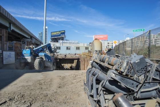 Tunnel boring machine conveyor system being transported on 4th Street in SoMa with blue crane and construction equipment visible.