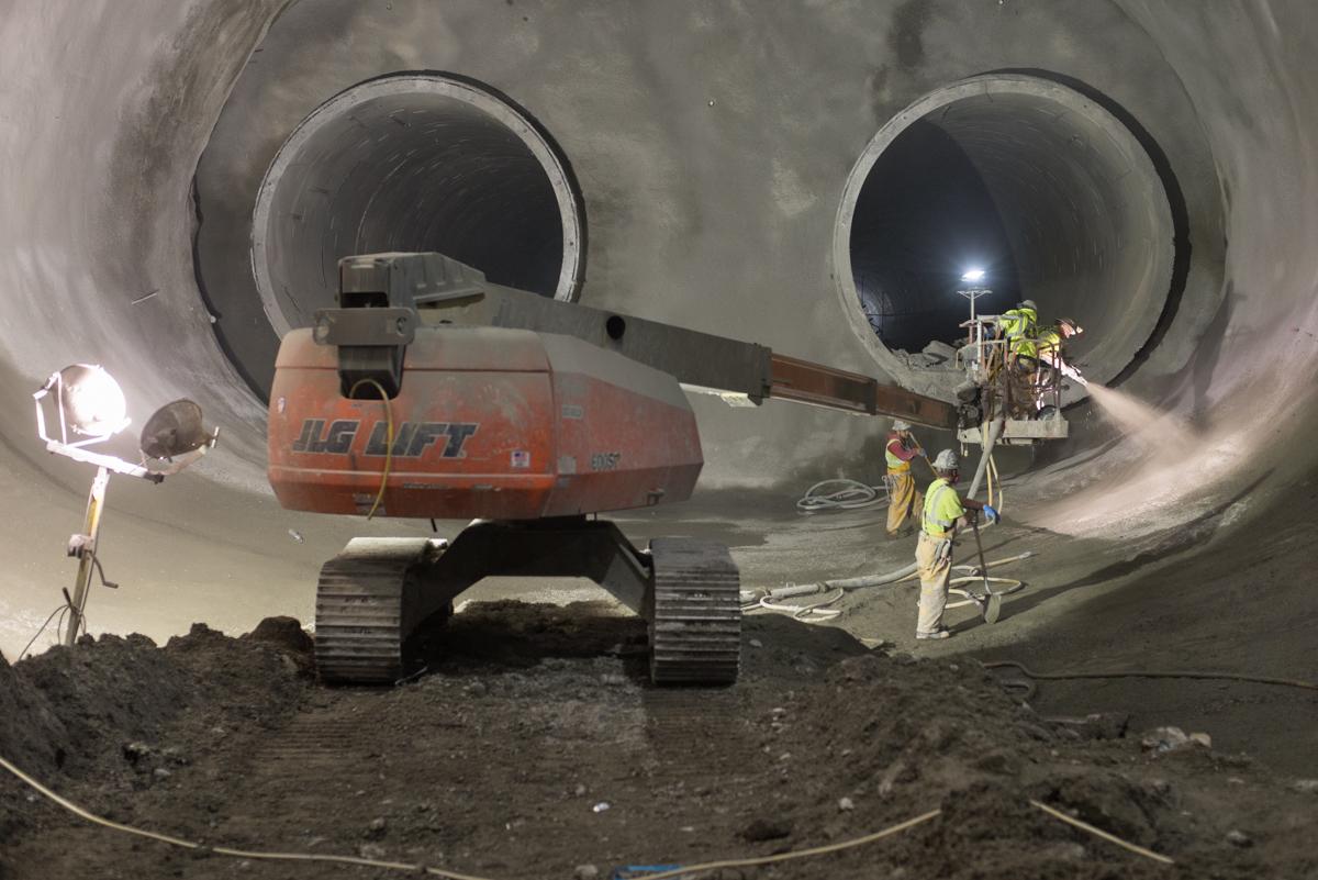 Workers in safety gear inside large concrete tunnel sections during underground transit construction.