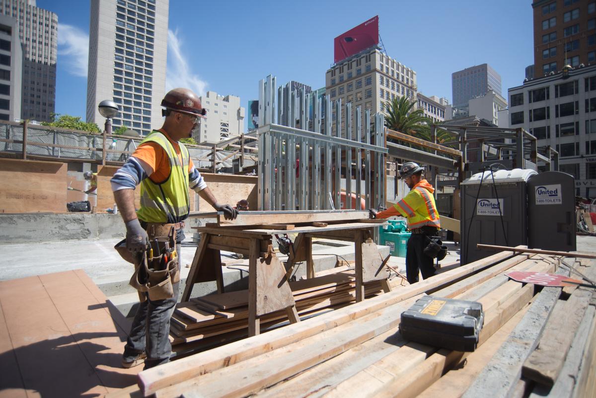 Construction workers assemble wooden forms on a rooftop at Union Square station entrance site.