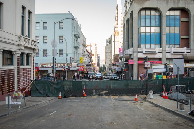 Construction site on Washington Street with green barriers, traffic cones, and urban buildings in background.