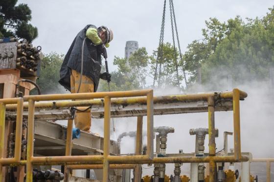 Worker pressure washing tunnel boring machine equipment with yellow safety railing visible.