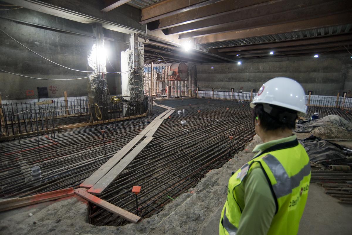 Construction worker in safety gear observing reinforced concrete floor preparation beneath Stockton Street station.