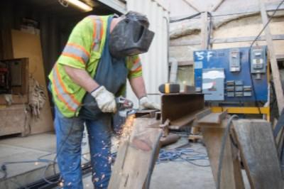 Worker in safety gear grinding steel beam at construction site