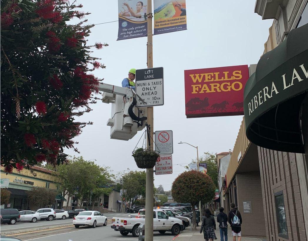 Worker in lift installing Muni taxi-only sign on West Portal Avenue street pole.