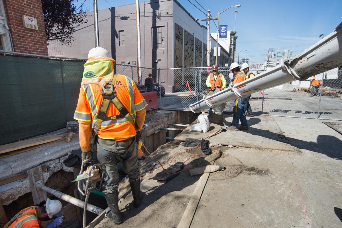 Construction workers in safety gear prepare concrete pour at 4th Street subway station construction site.