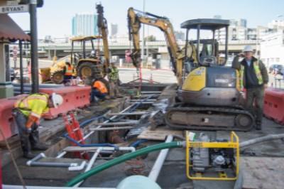 Construction crew operates excavators and equipment on urban street at night for utility work.