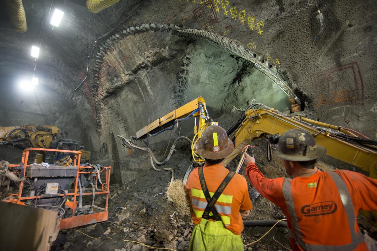 Workers in safety gear operate excavation equipment inside an underground tunnel during construction.