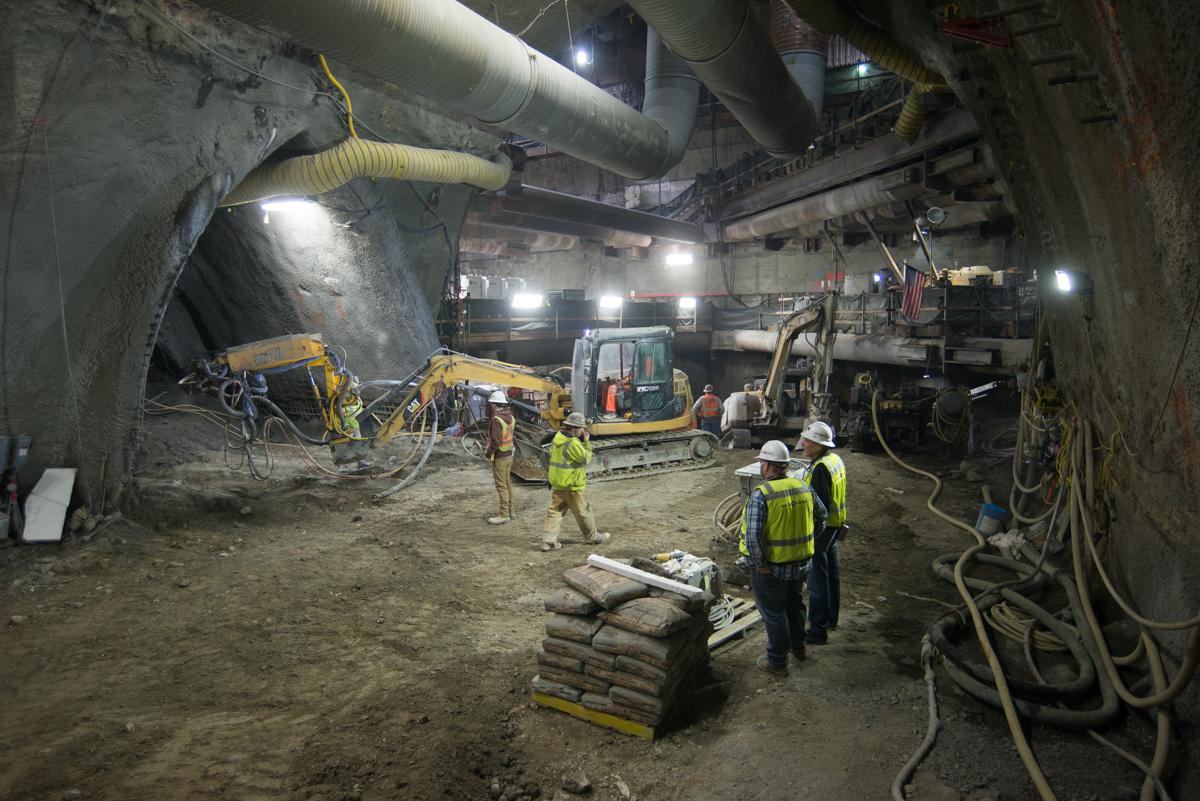 Workers in safety vests operate equipment during underground tunnel excavation and construction.